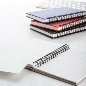 A stack of spiral-bound notebooks in blue, red, black, and white, with one opened to reveal lined pages.