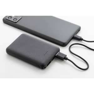 A black 5000mAh recycled ABS power bank with a mobile phone, both connected with a charging cable.