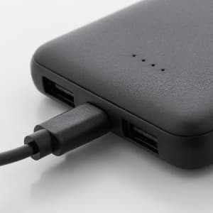 A black power bank with USB ports and a charging cable connected, made from recycled ABS material.