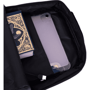 An open black backpack features a book and a phone inside a compartment, with a charging cable visible.