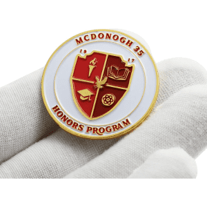 A gold and red enamel lapel pin featuring a shield design held on a white background.