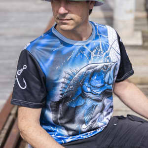 A fishing tee featuring a blue and black design with a graphic of a fish, worn by a person outdoors.