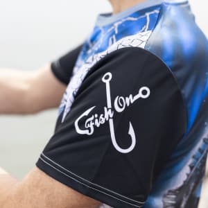 A men's fishing tee in blue and black with a fishing hook design on the sleeve and logo branding.