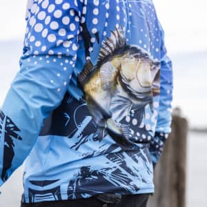 A blue long sleeve fishing tee with a fish graphic and abstract patterns, featuring a logo on the back.