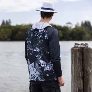 A men's polyester sublimated 1/4 zip fishing hoodie in navy and grey, featuring a hood and a logo, worn by a person by the water.