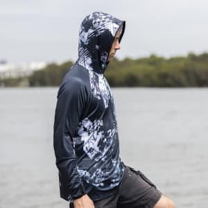 A men's polyester sublimated 1/4 zip fishing hoodie in dark blue with a graphic pattern, worn by a person by the water.