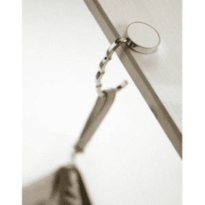 A silver bag hanger attached to a table edge, featuring a circular base and chain link design.