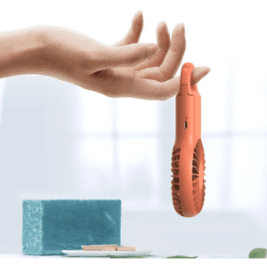 A handheld, coral pocket fan is suspended above a blue sponge and a dish, with a soft background.
