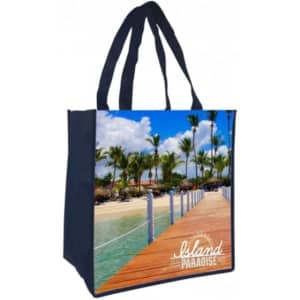 A navy tote bag featuring a vibrant beach scene with palm trees and a wooden boardwalk, including a logo.
