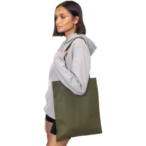 A woman in a grey hoodie carries an olive green tote bag. The bag has shoulder straps and a simple design.