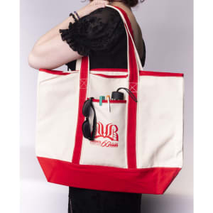 A large canvas tote bag in cream and red, featuring a logo and holding sunglasses and a drink bottle.