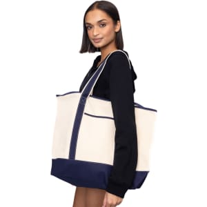 A model holds a large beige and navy tote bag with a sturdy design and visible branding.