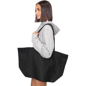 A woman holds a large black canvas tote bag over her shoulder, featuring a simple design and sturdy handles.