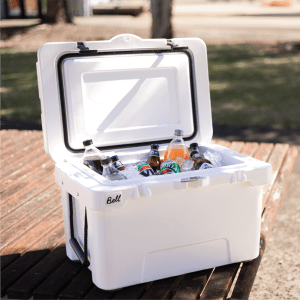 A white cooler box opened to reveal assorted drinks, including bottles and cans, resting on a wooden surface.