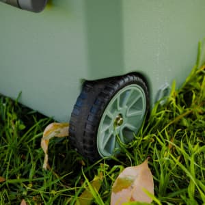 A grey cooler box on grass, featuring a sturdy wheel for mobility, surrounded by fallen leaves.