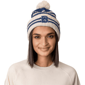 A beanie hat in white and navy, featuring a pom pom on top and a logo, worn by a model.
