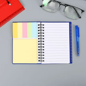 A blue mini notebook with a ballpoint pen, featuring lined pages and sticky notes in pastel colours, alongside glasses and a ruler.