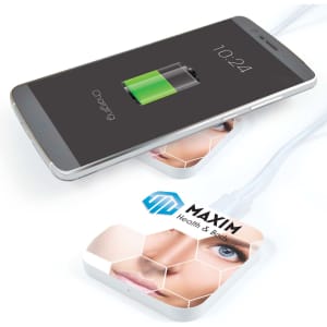 A white wireless charger with a design featuring a face, placed under a smartphone displaying a charging icon.