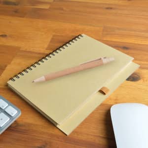 A Savannah Notebook with a spiral binding sits on a wooden surface next to an Eco Matador Pen.