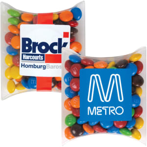A pillow pack containing colourful chocolate beans, including red, yellow, blue, green, and brown candies, with branding visible.
