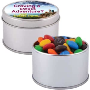 A silver round tin filled with colourful M&M's, including red, yellow, blue, green, and brown candies.
