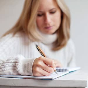 A bamboo pen is being held by a person who is writing in a notebook.