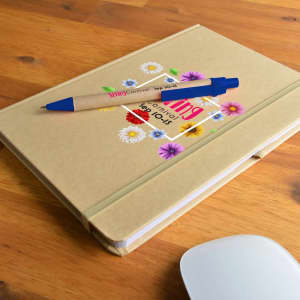 A tan A5 notebook with floral designs and a blue pen resting on top, placed on a wooden surface.