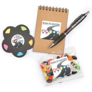 A notebook, a colorful sticky note pad, a pen, and a bag of assorted jelly beans, all featuring a logo.
