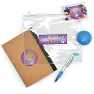 A clear zipper pouch, a brown notebook, a blue stress ball, and a pen, along with a packet of colorful candies.