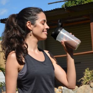 A drink bottle with a black lid and a clear body, held by a person outdoors, featuring a logo.
