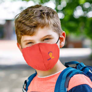 A children's face mask in bright red with a logo, worn by a boy in an outdoor setting.