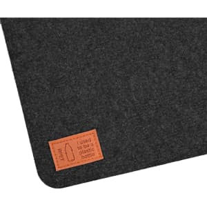 A dark felt desk mat with a stitched leather tag that reads "I used to be a plastic bottle."