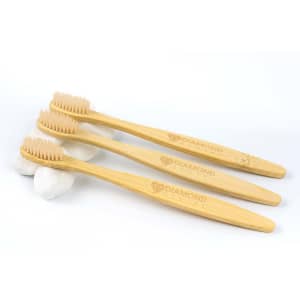 Three bamboo toothbrushes with light brown bristles, placed on smooth white stones. The handles feature a logo.