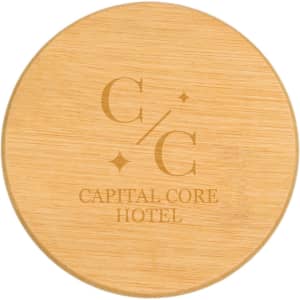 A round bamboo coaster featuring a logo and text for "Capital Core Hotel". The surface is smooth and natural in texture.