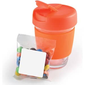 A reusable coffee cup in orange with a matching lid, accompanied by a bag of colorful M&M's.