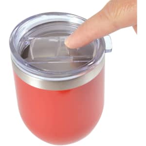 A reusable coffee cup in a vibrant red color with a silicone lid and a metallic band, featuring a finger pressing the lid.
