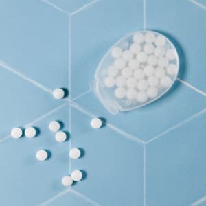 An egg-shaped container holds white sugar-free breath mints, with some mints scattered on a blue background.