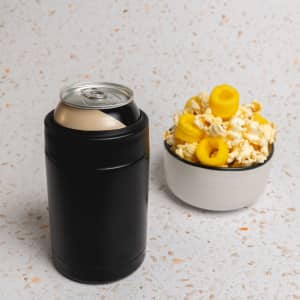 A drink bottle in black stainless steel beside a bowl of popcorn topped with yellow snacks. The image includes branding.