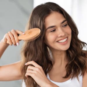 A bamboo hair brush featuring a wooden handle, being used by a woman with wavy brown hair.