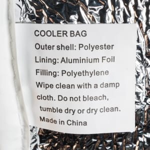 A silver cooler bag, featuring a polyester outer shell and aluminium foil lining, with a label detailing care instructions.