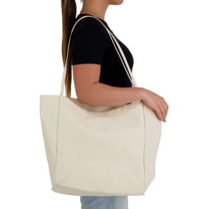 A spacious cream tote bag with long straps, held by a person against a plain background.
