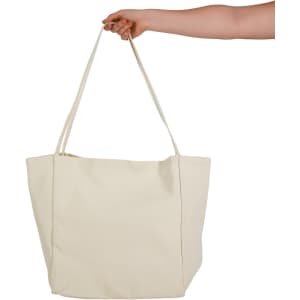 A hand holds a large, cream-coloured tote bag with two long handles and a simple design.