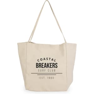 A cream tote bag with a logo featuring the text "Coastal Breakers Surf Club" and a date.