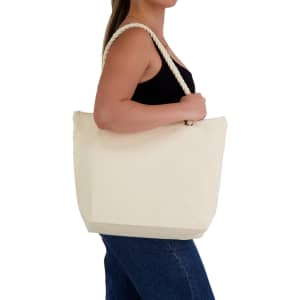 A cream-coloured canvas tote bag with rope handles, held by a person in a black top and blue jeans.