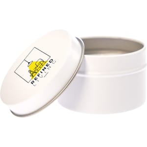 A white tin candle with a metal lid, featuring a logo on the top. The candle is unlit and inside the tin.