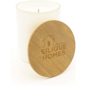 A medium glass candle with a white body and a wooden lid, featuring a logo on the lid.