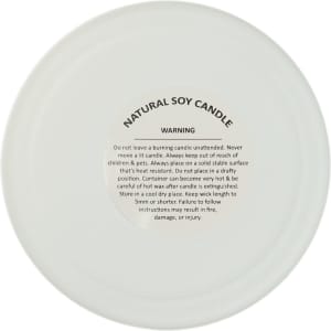 A natural soy candle with a warning label on the bottom, detailing safety instructions.