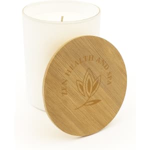 A large white glass candle with a wooden lid, featuring a logo and an embossed design on the lid.