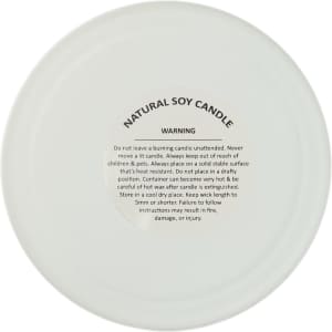 A large white glass candle with a frosted finish and a warning label on the base, featuring natural soy wax.