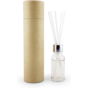 A clear glass reed diffuser bottle with a silver cap and white reeds, packaged in a brown cylindrical box.